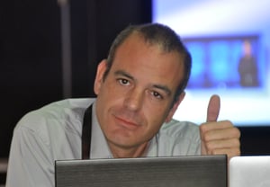 Profile photo of a man in a grey shirt sitting behind the laptop screen