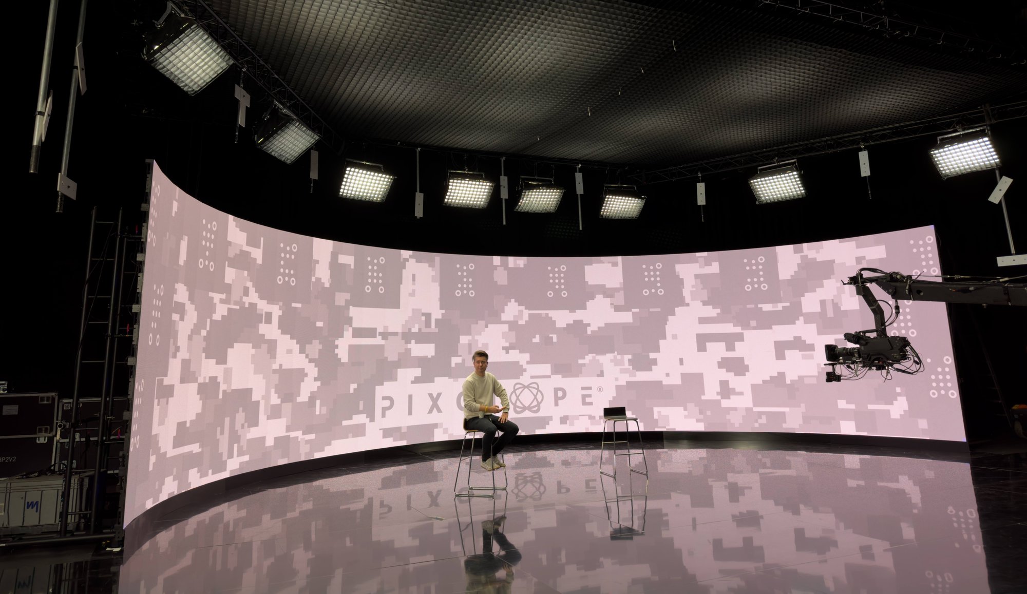 A host sitting on a chair in the studio with a large LED volume behind his back